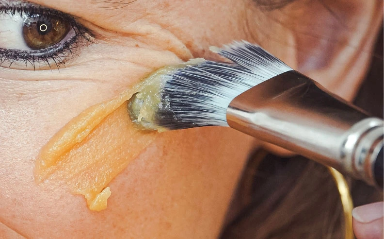Zoom sur la pommette d'une femme qui s'applique le masque réparateur au miel
